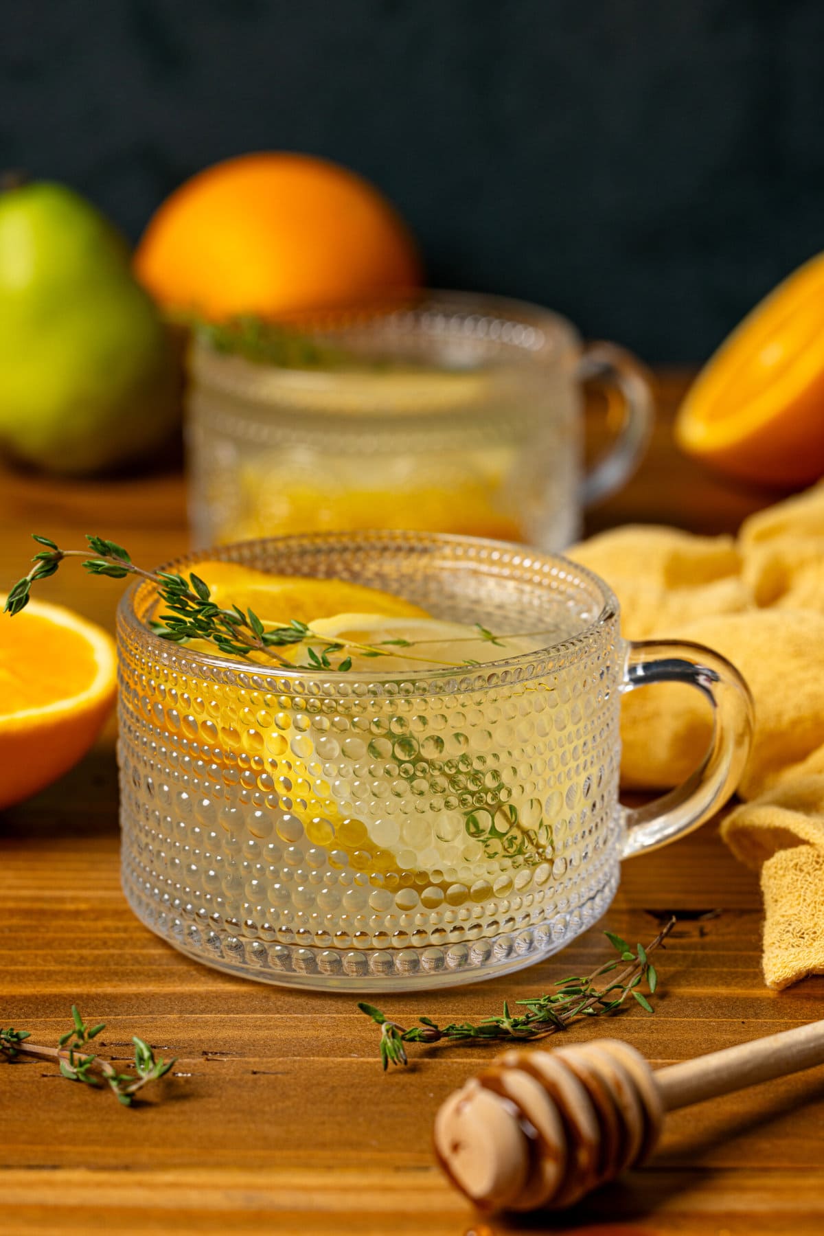 Two mugs of tea on a brown wood table with oranges and pears.