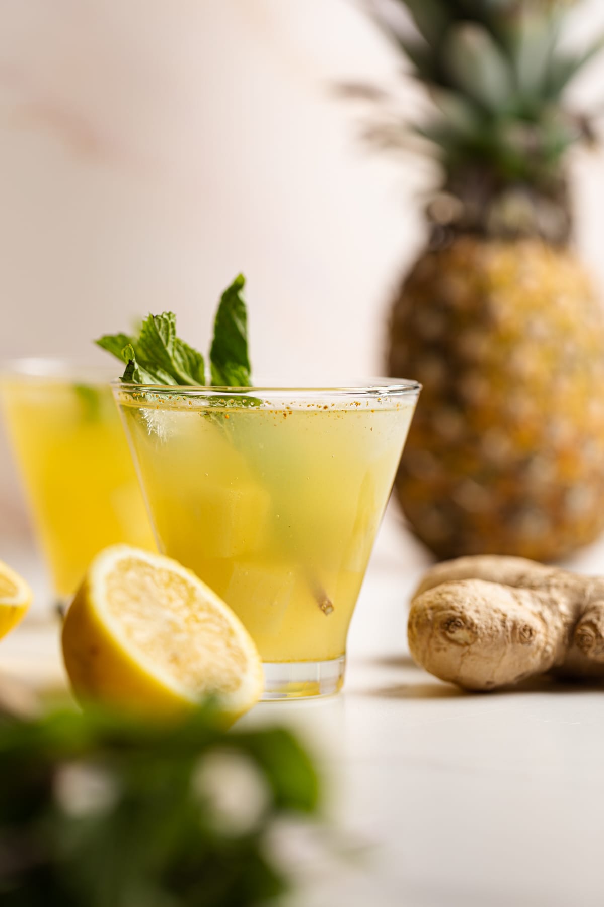 Glasses of Pineapple Ginger Turmeric Lemonade on a table with ginger, lemons, and a pineapple.