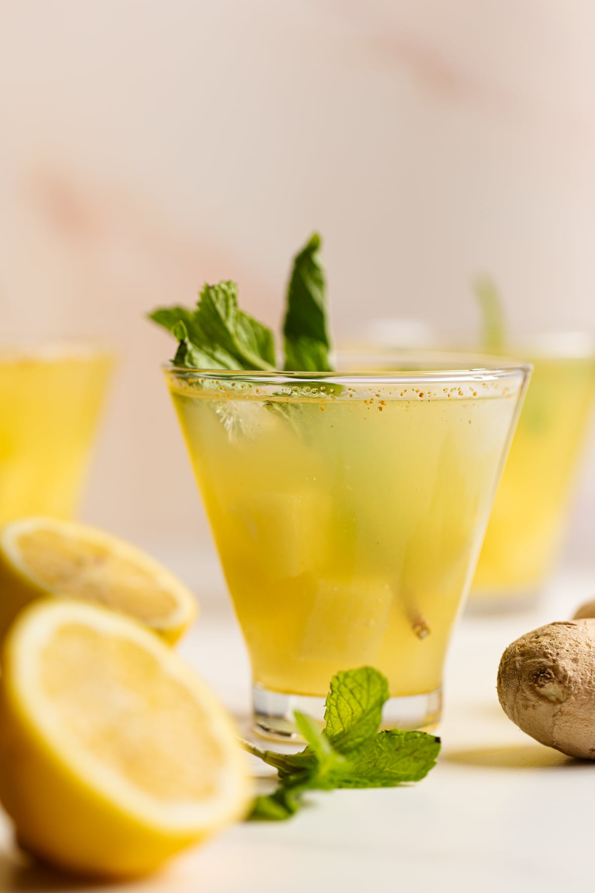 Glass of Pineapple Ginger Turmeric Lemonade surrounded by mint, lemons, and ginger.