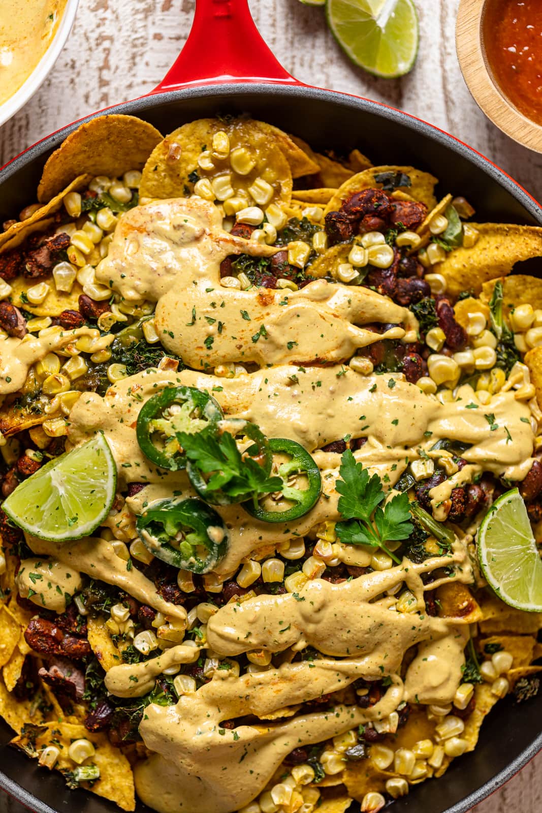 Closeup of Loaded Vegan Queso Skillet Nachos topped with jalapeno slices and lime wedges