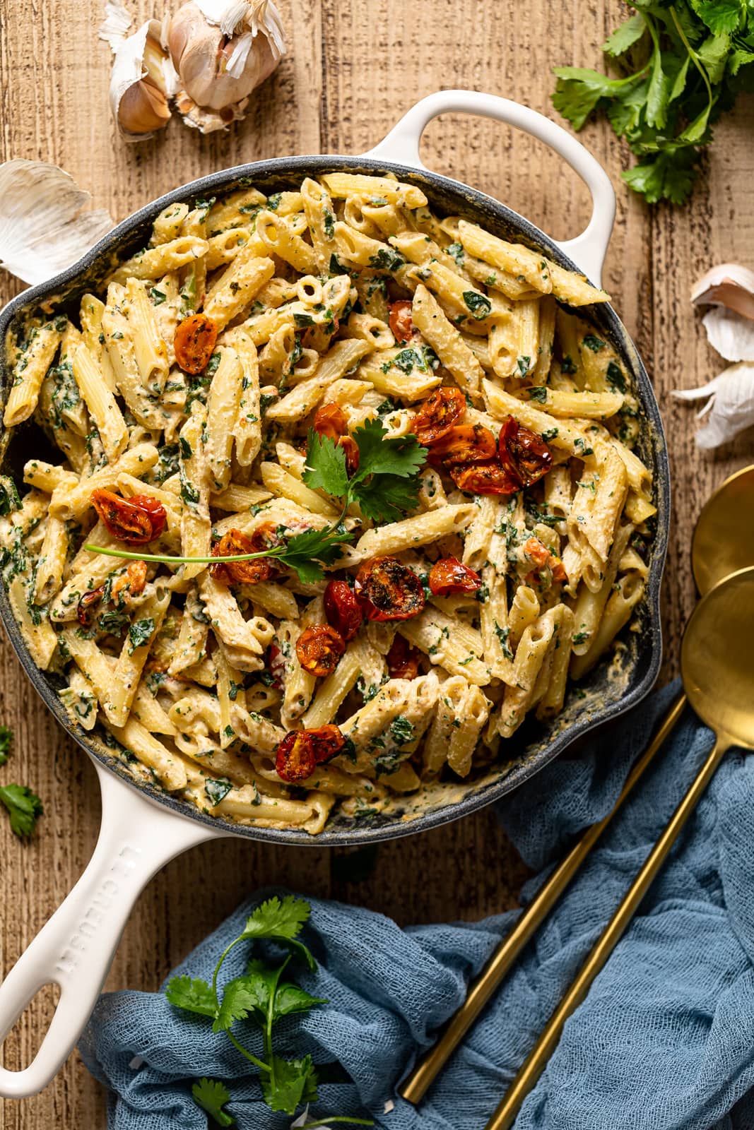 Overhead shot of Creamy Vegan Tuscan Kale Pasta next to garlic, parsley, and serving spoons