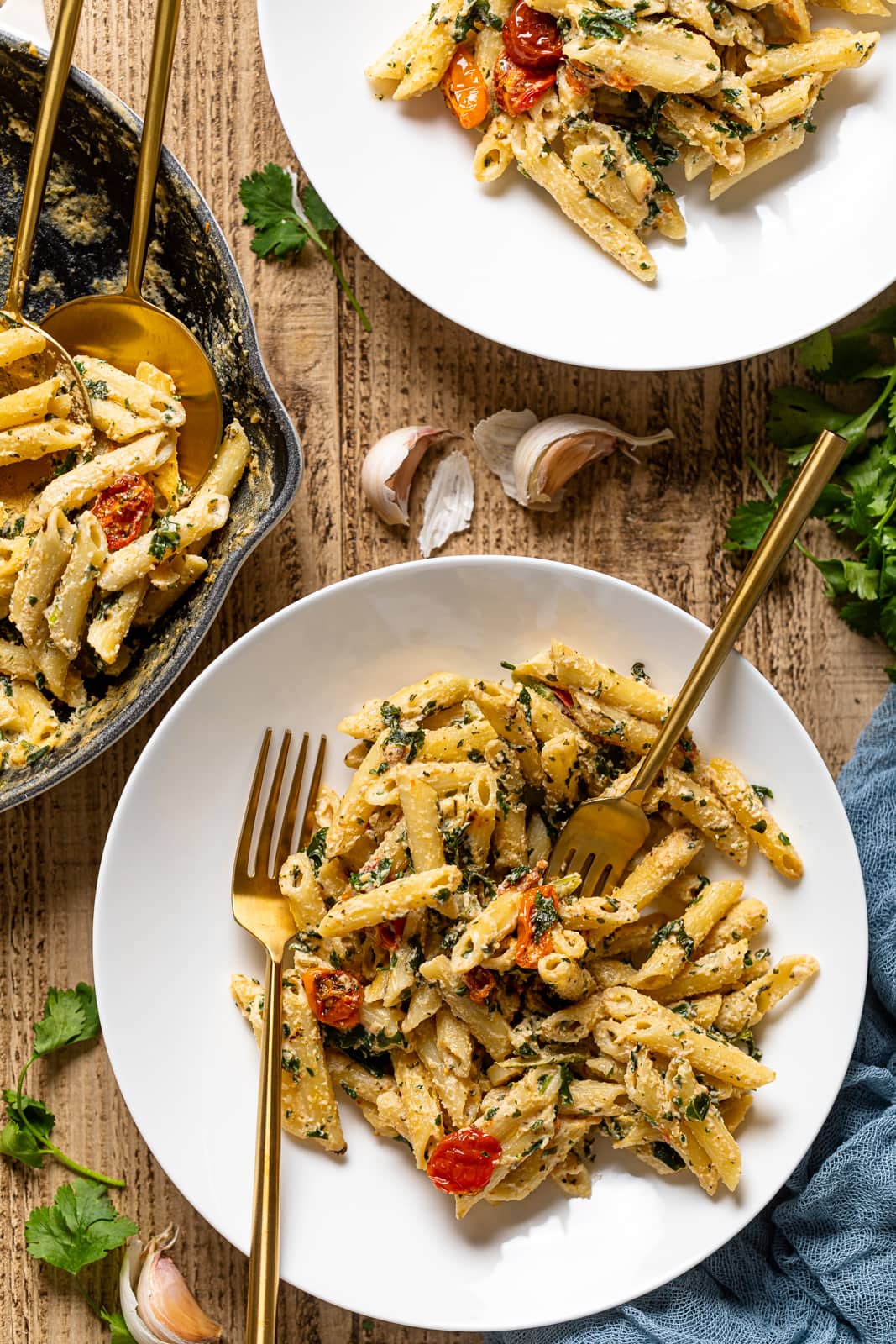 Overhead shot of two plates and a skillet of Creamy Vegan Tuscan Kale Pasta