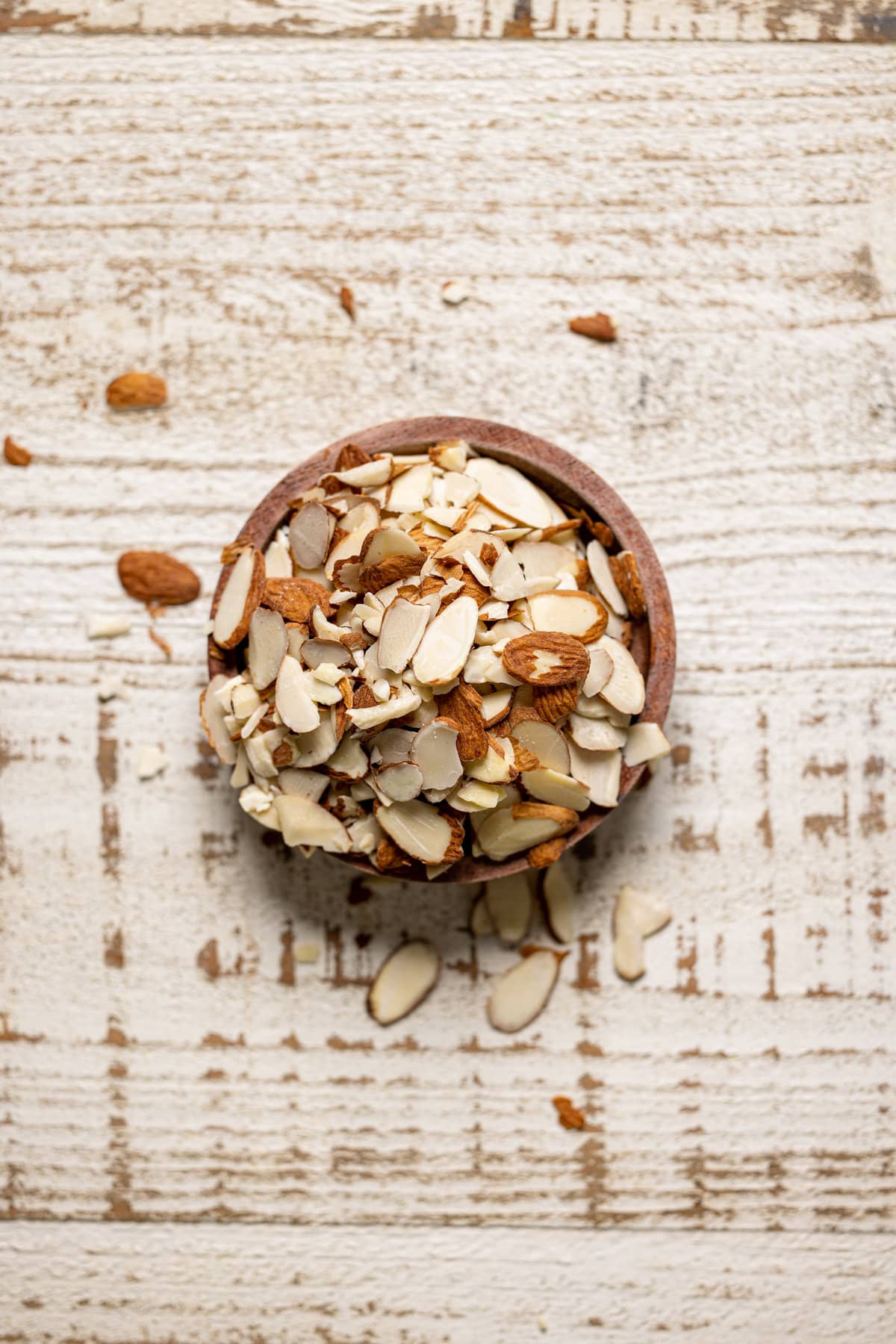 Bowl of slivered almonds on a white, wooden table.