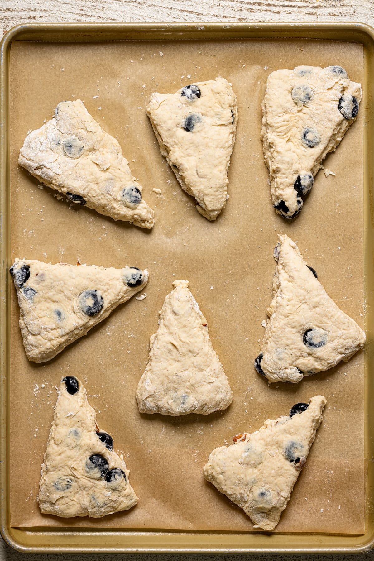 Uncooked Dairy-Free Blueberry Almond Scones on a lined baking sheet.