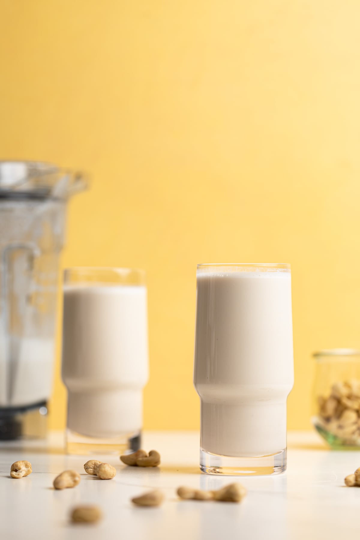 Two tall glasses of Creamy Cashew Milk against a yellow background