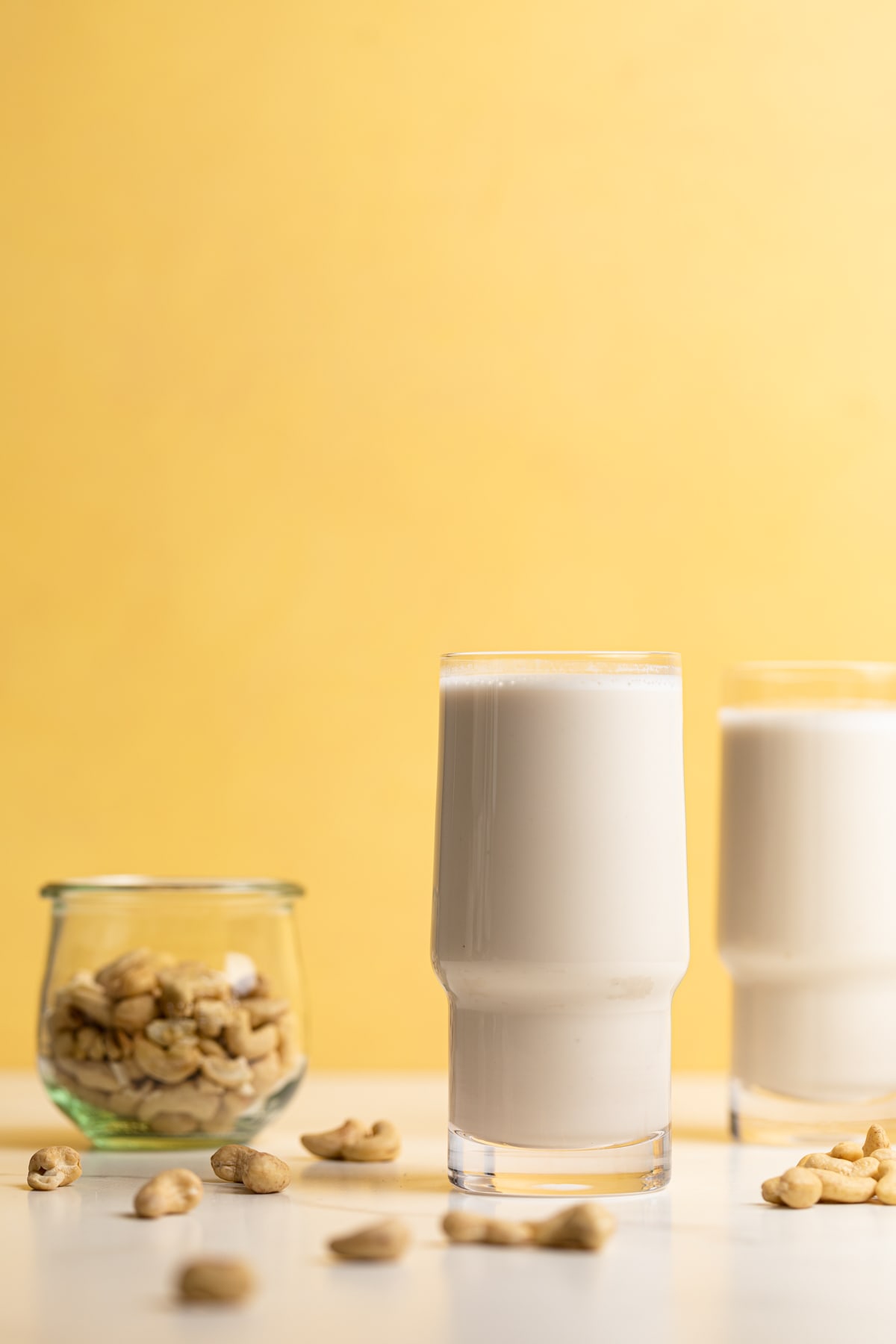 Two tall glasses of Creamy Cashew Milk next to a bowl of cashews