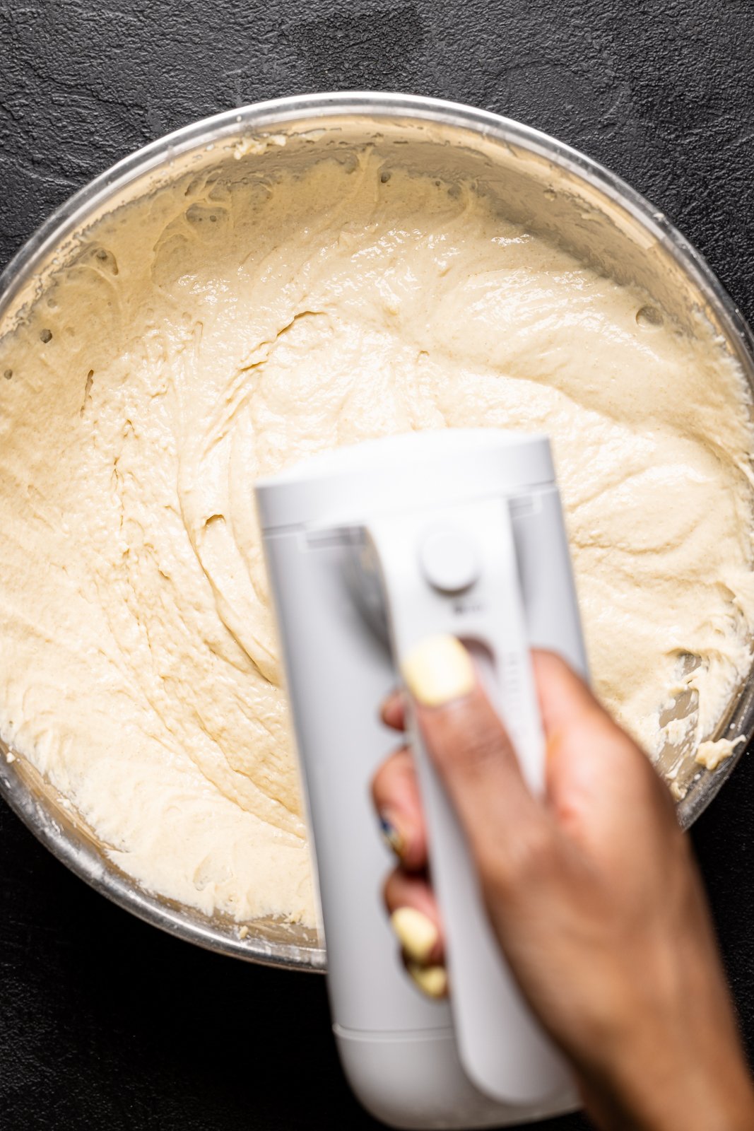 Cake batter being mixed in a white bowl with an electric hand-mixer.