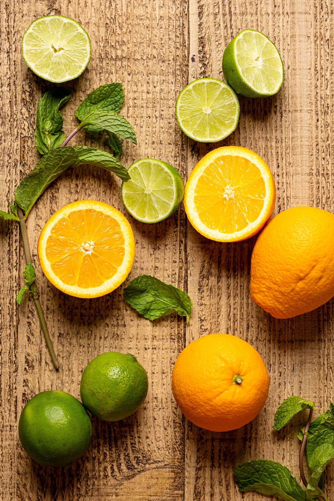 Slices of oranges, limes, and mint leaves, on a brown wood table.