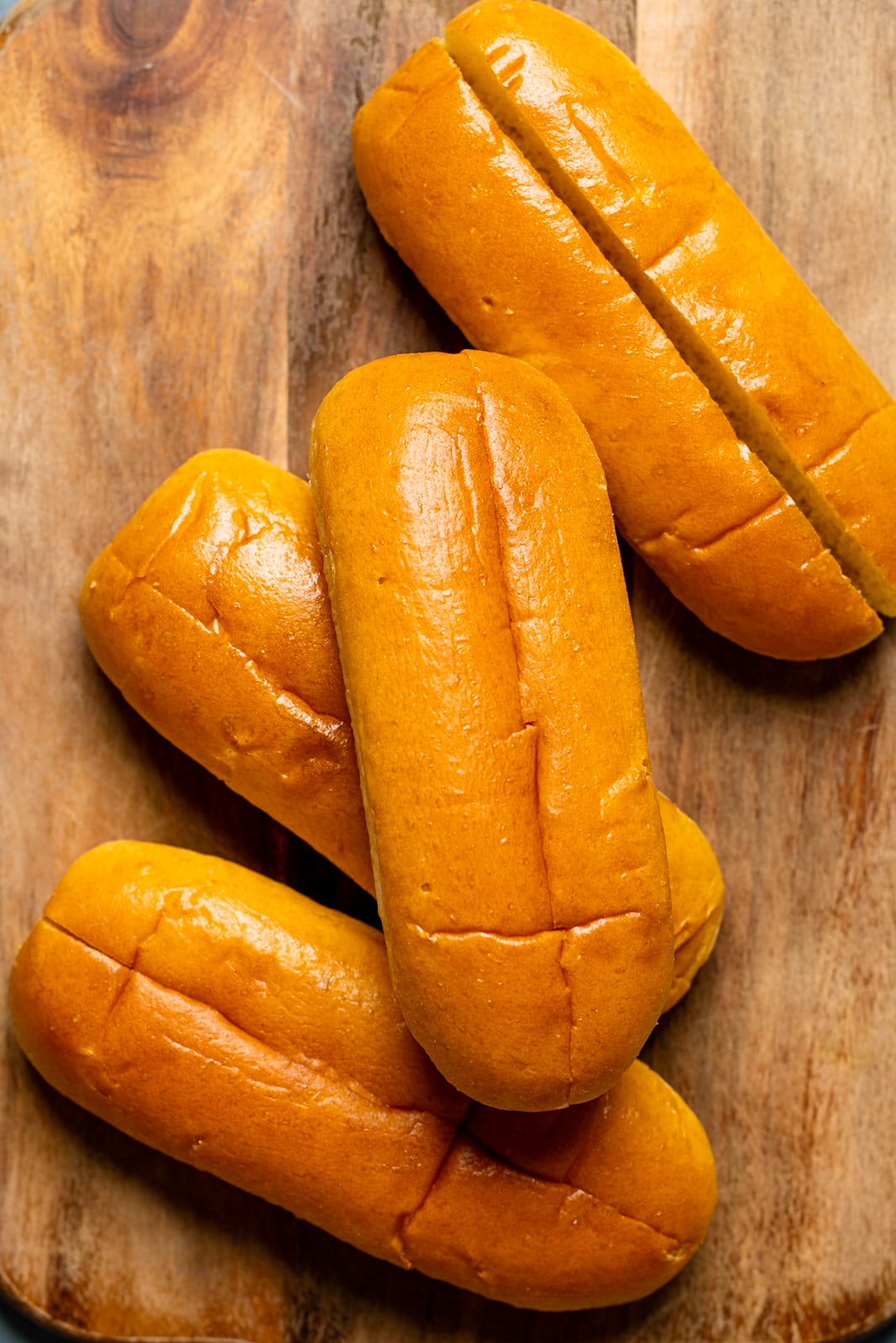 Hot dog buns on a brown wood cutting board.