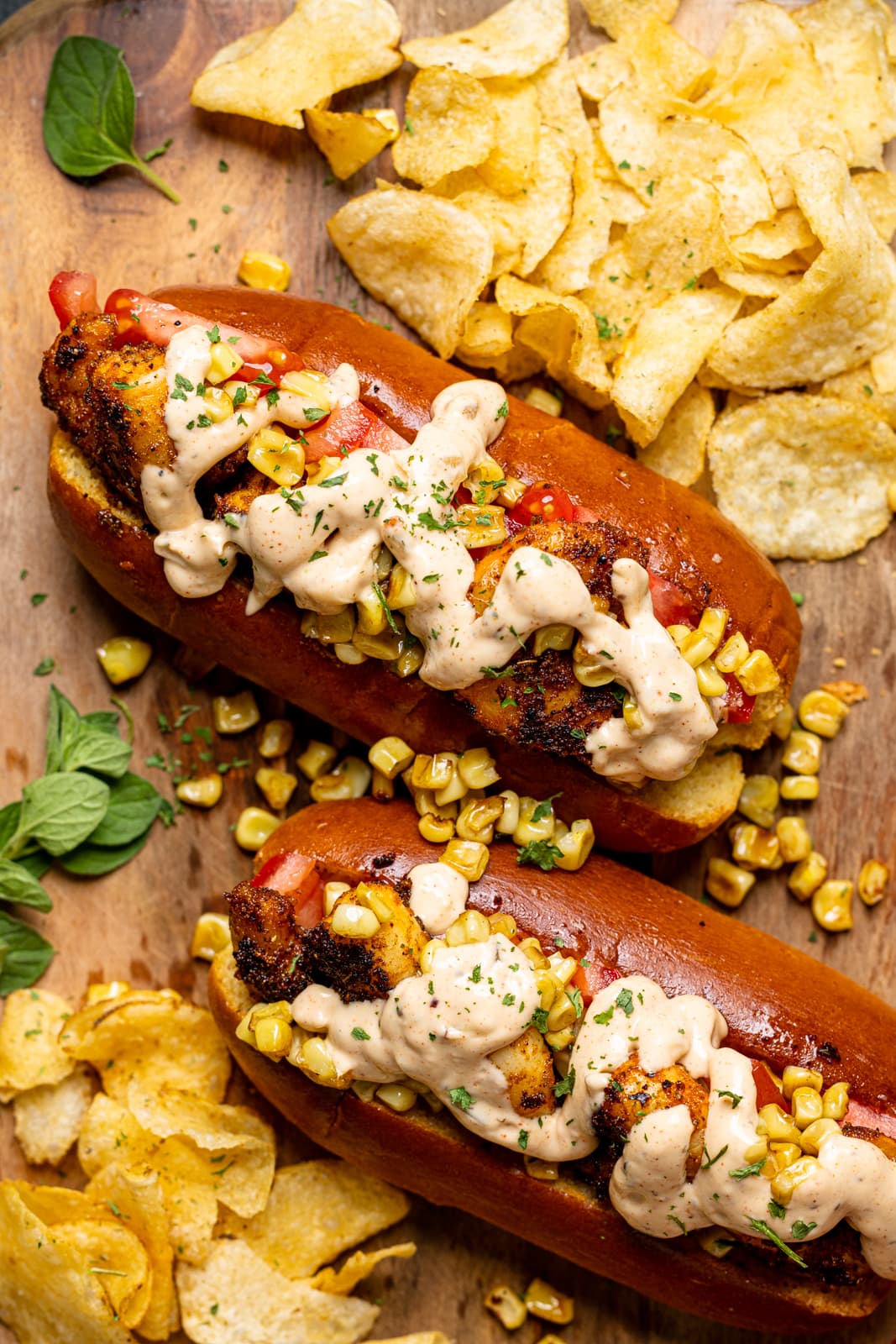 Up close shot of po' boy sandwiches on a brown wood cutting board with a side of chips.