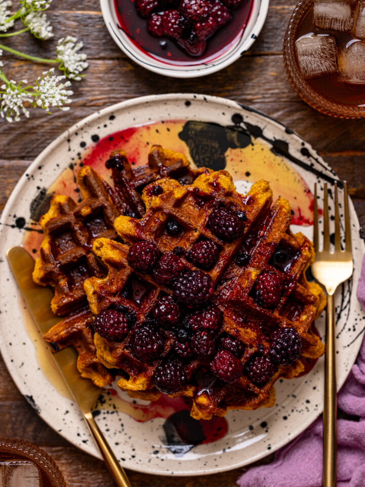 Up close shot of sweet potato waffles on a plate with utensils and drinks.