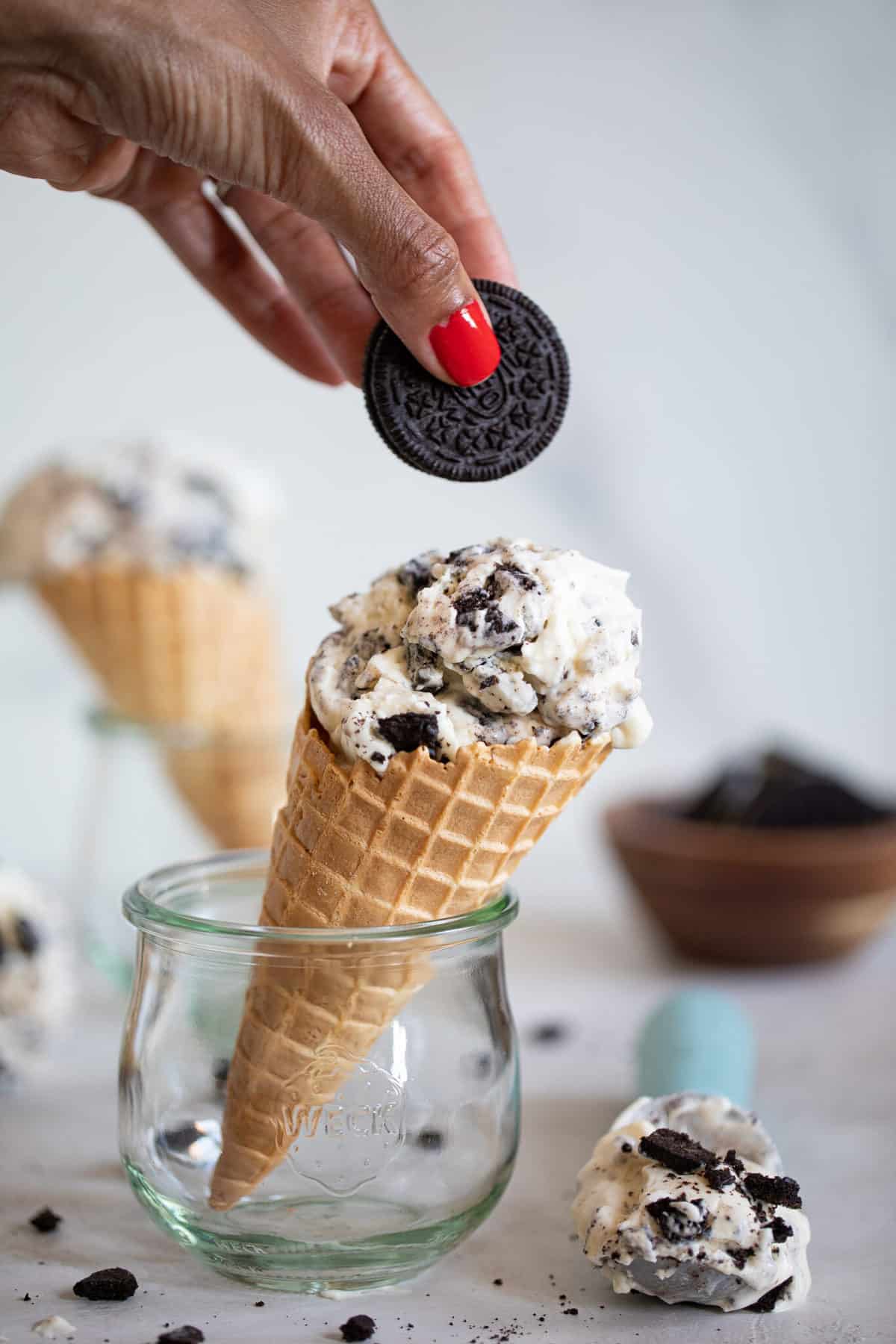 Woman adding an Oreo to a cone of No-Churn Cookies and Cream Ice Cream.