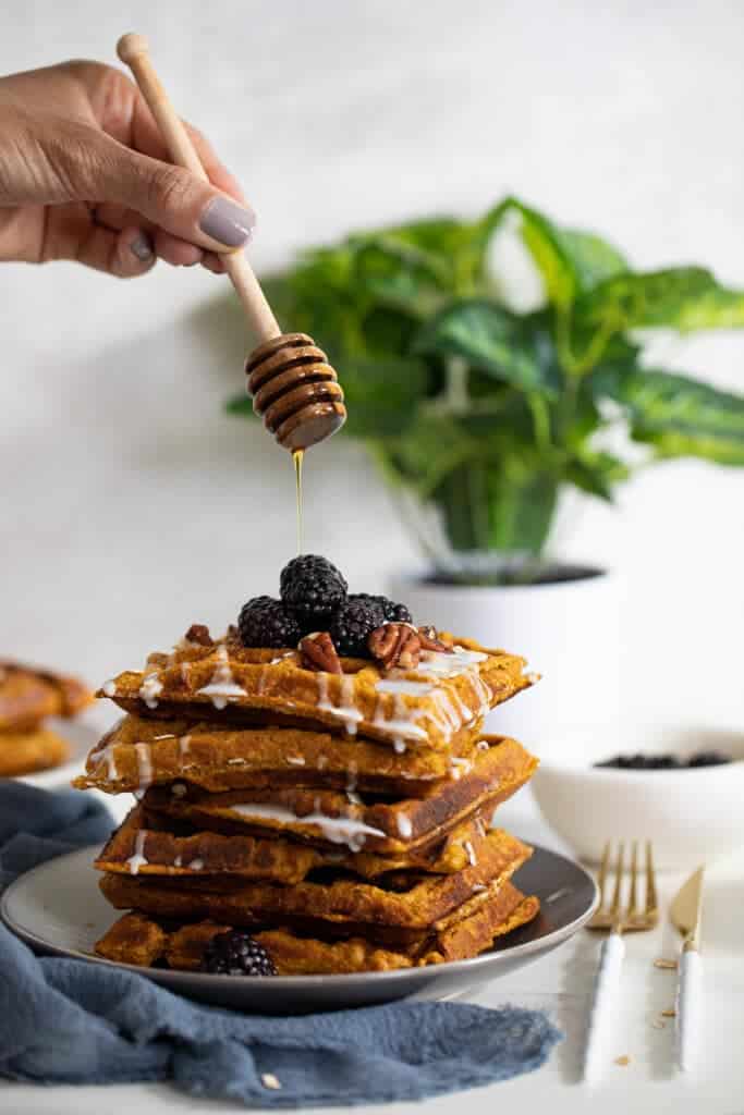 Woman dripping honey onto a stack of Flourless Vegan Sweet Potato Oats Waffles.