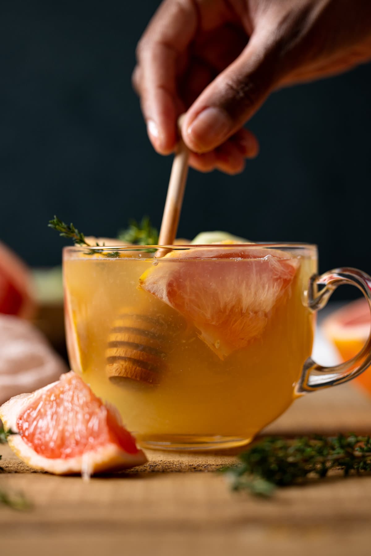 Hand stirring Honey Grapefruit Cucumber Thyme Tea with a honey dipper