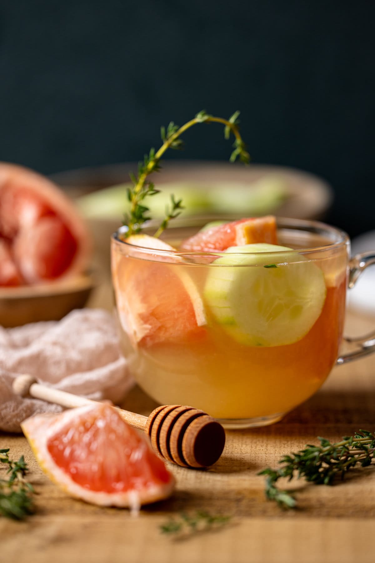Glass of Honey Grapefruit Cucumber Thyme Tea next to a honey dipper