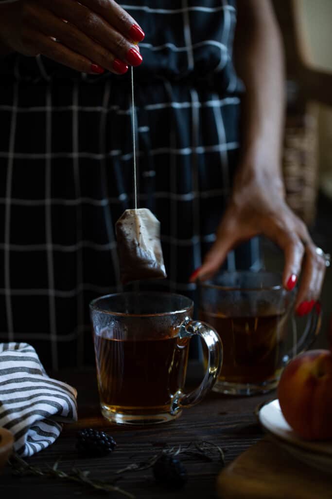 Woman pulling a tea bag from a glass mug.