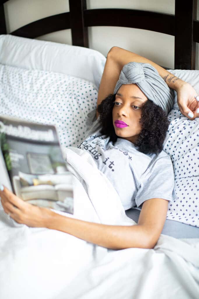 Shanika lying in bed reading a Crate & Barrel magazine.