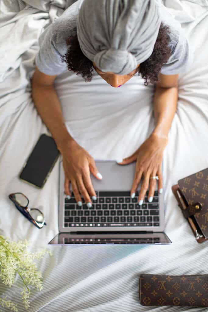 Shanika typing on a laptop while sitting in bed.