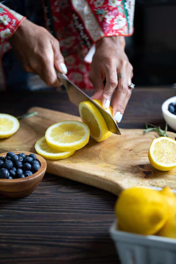 Woman slicing a lemon on a wooden board.