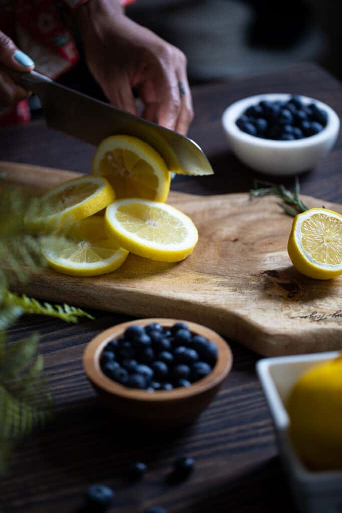 Woman slicing a lemon on a wooden board.