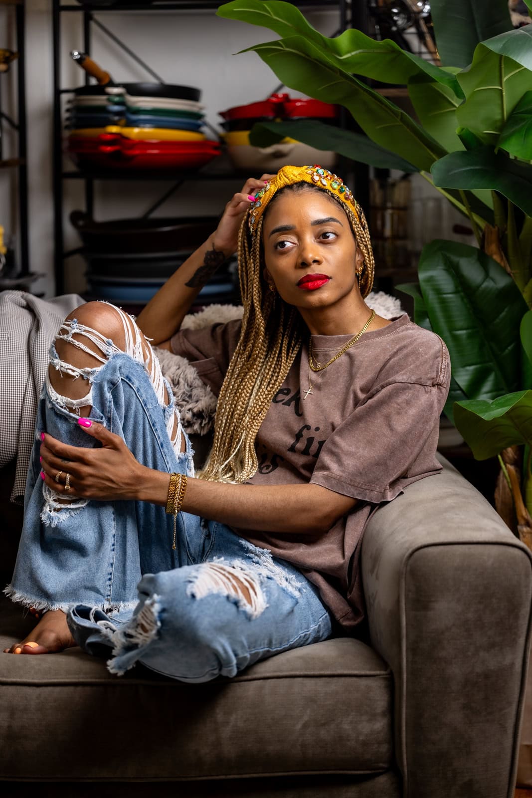Shanika sitting on couch with jeans and a brown shirt, holding leg and looking off to the side.