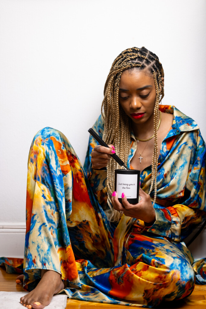 Shanika dressed in a colorful two piece outfit sitting on the floor looking down while lighting a candle.