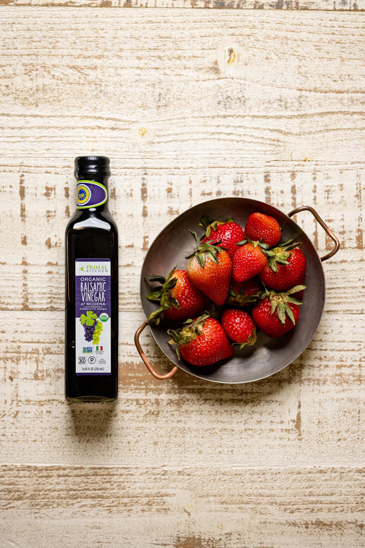 Container of strawberries next to a bottle of balsamic vinegar