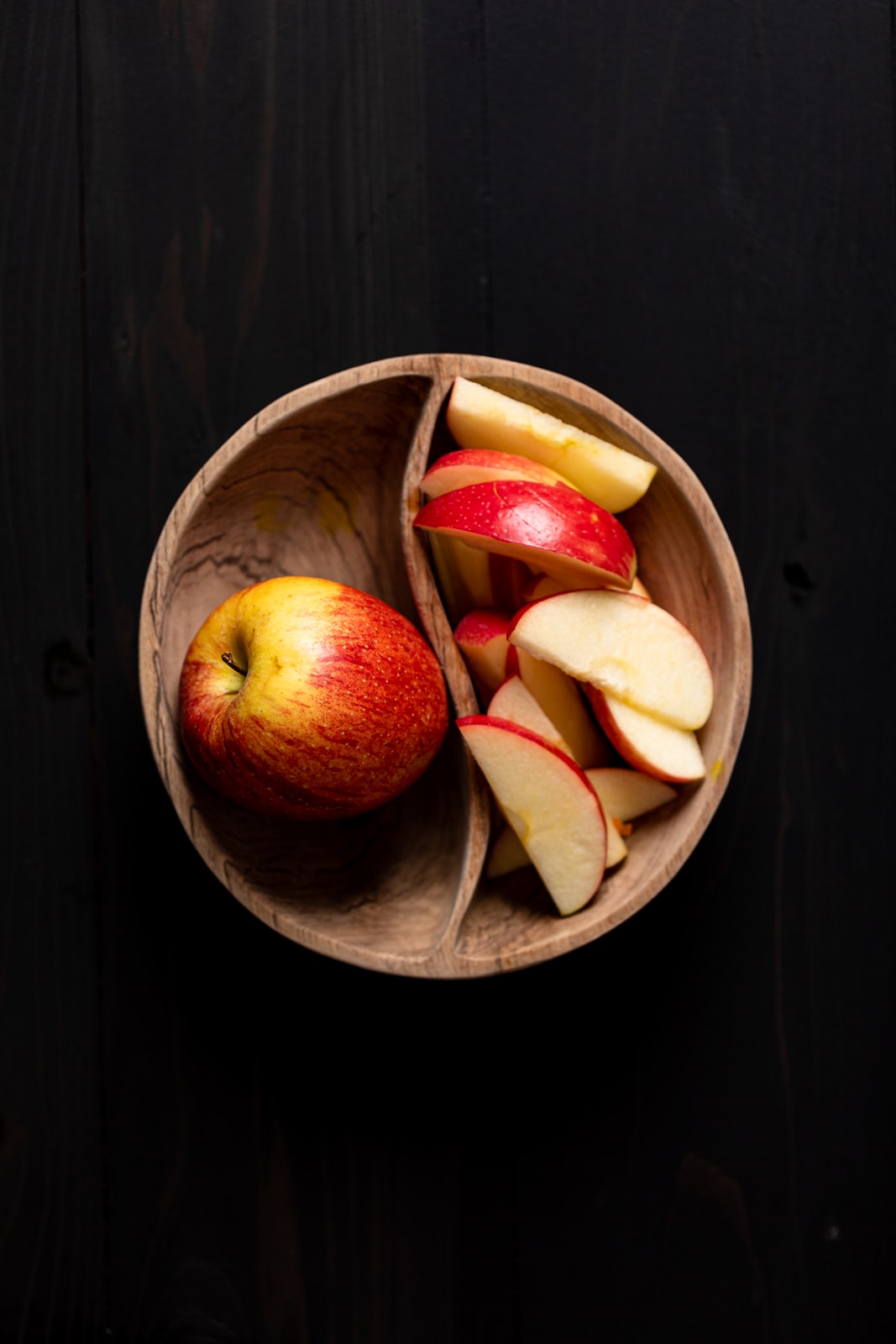 Whole apple and sliced apples in a wooden bowl.