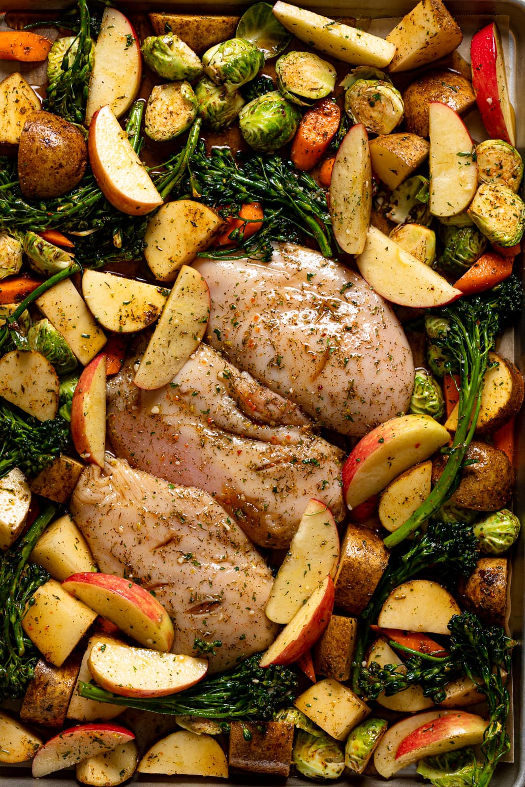 Uncooked Maple Apple Chicken and Veggies on a sheet pan.