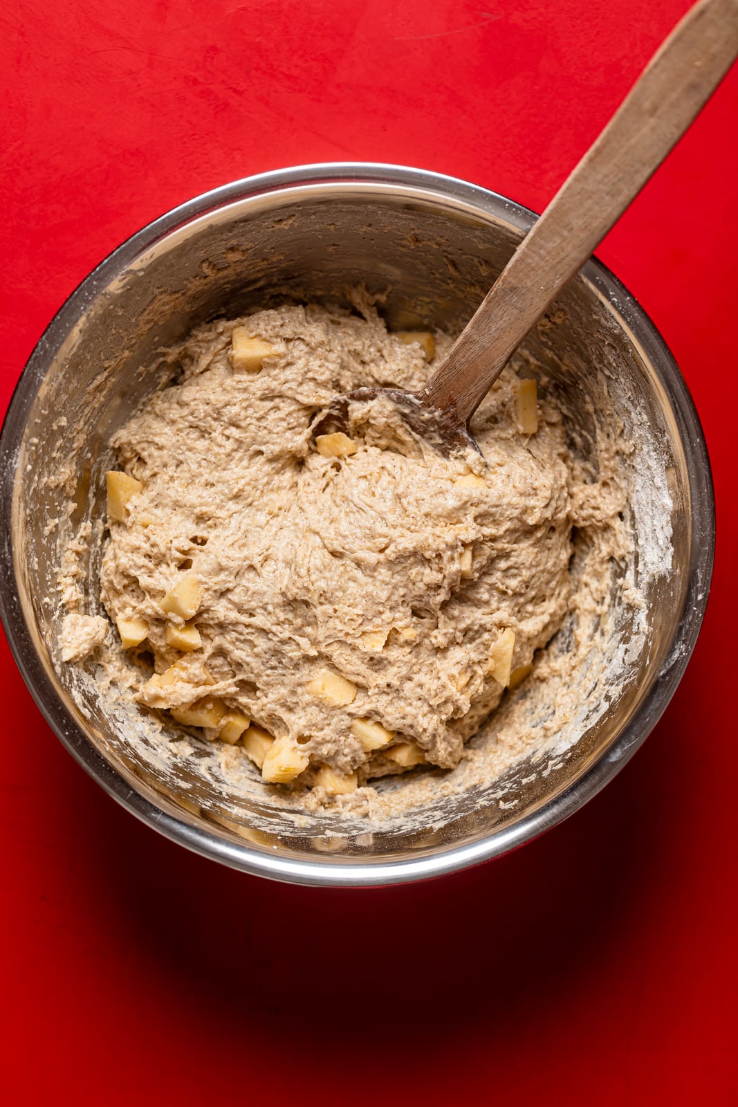 Wooden spoon stirring Vegan Apple Bread in a metal bowl.