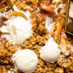 Up close shot of apple crisp with three scoops of ice cream and spoons.