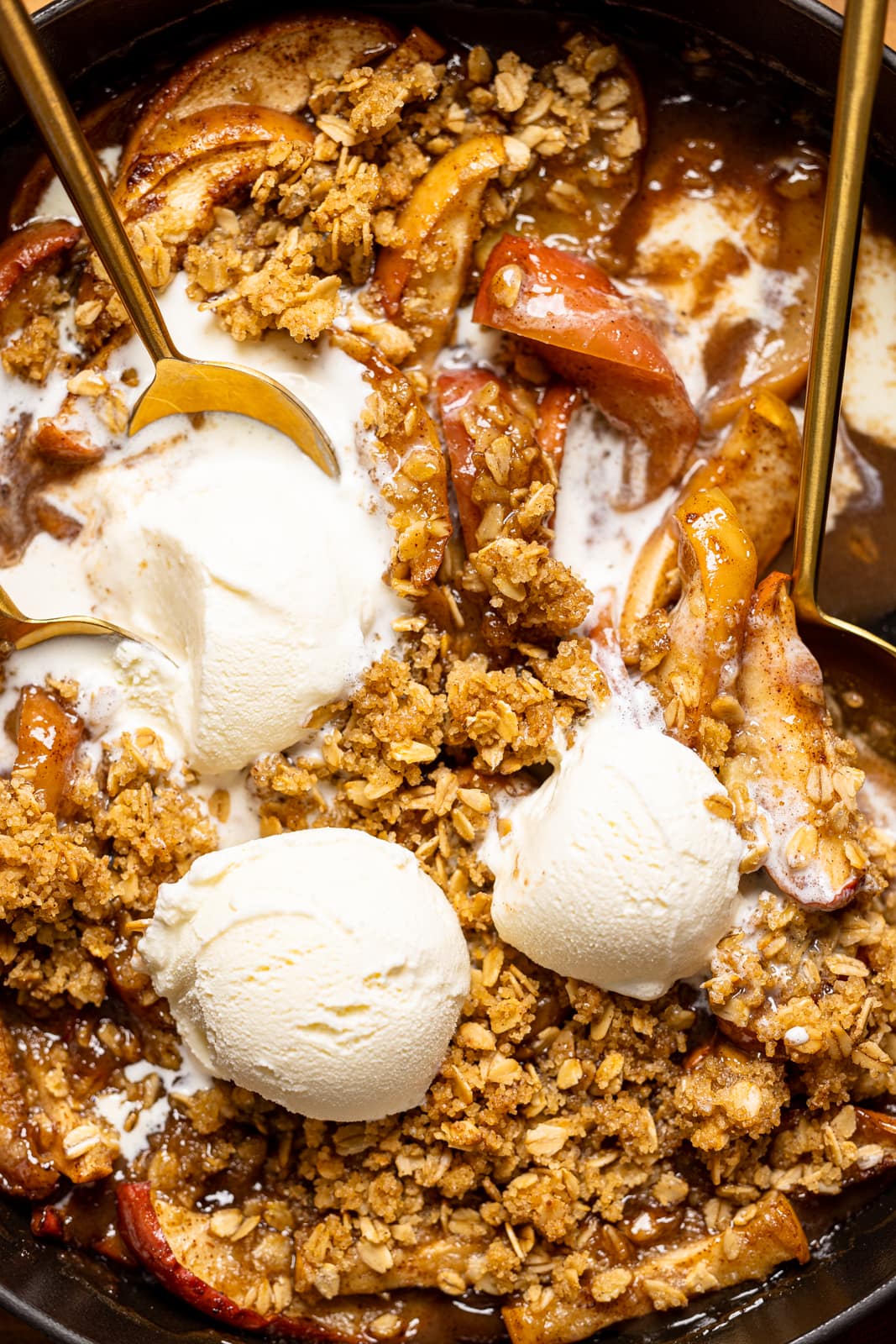 Up close shot of apple crisp with three scoops of ice cream and spoons.