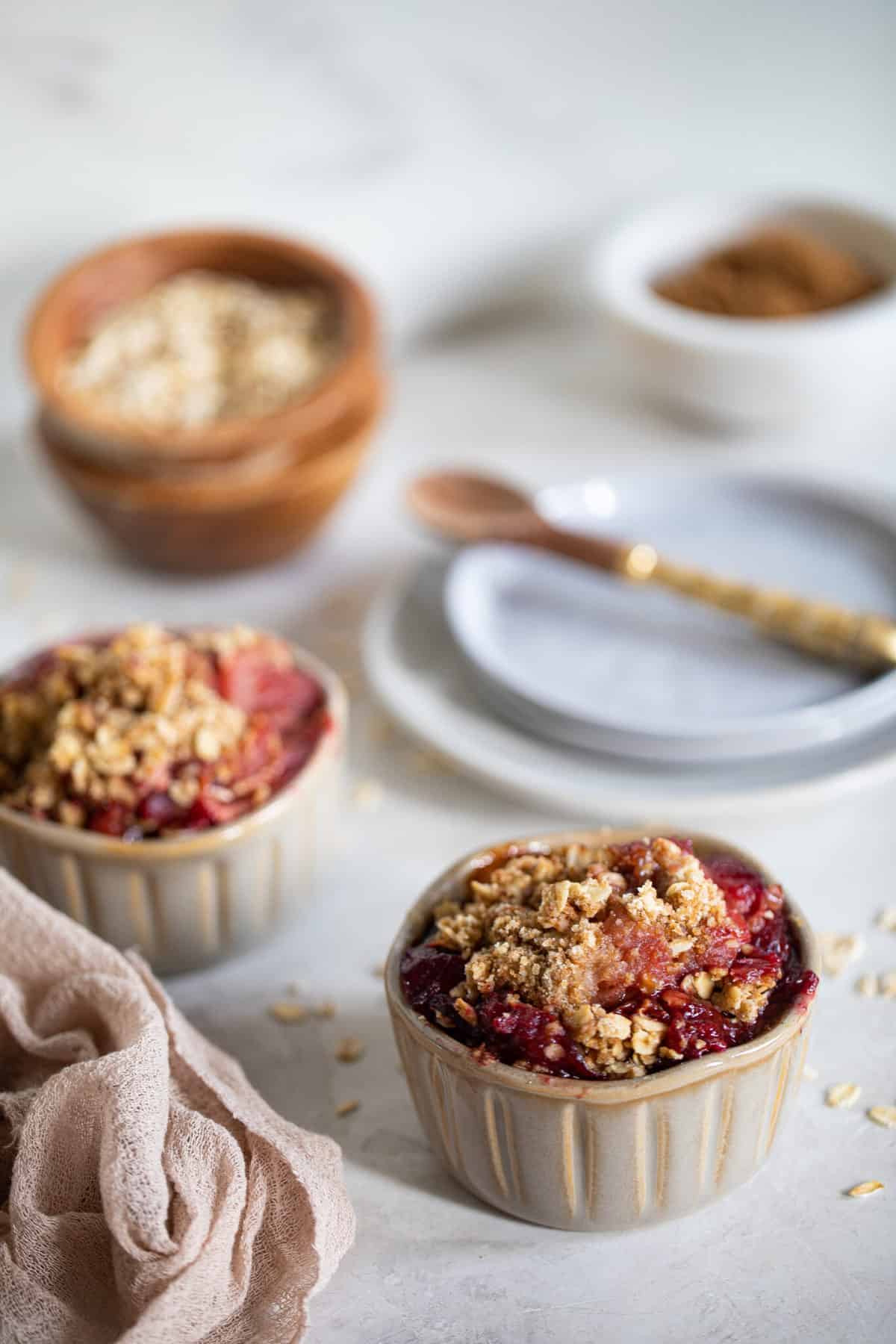 Table with bowls of Vegan and Gluten-Free Apple Plum Crisp and scattered oats.