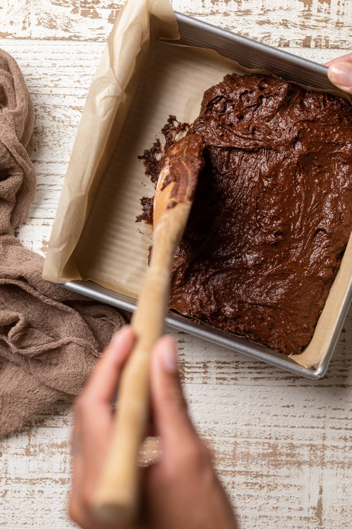 Wooden spoon spreading Extra Fudgy Vegan Brownie batter in a pan.