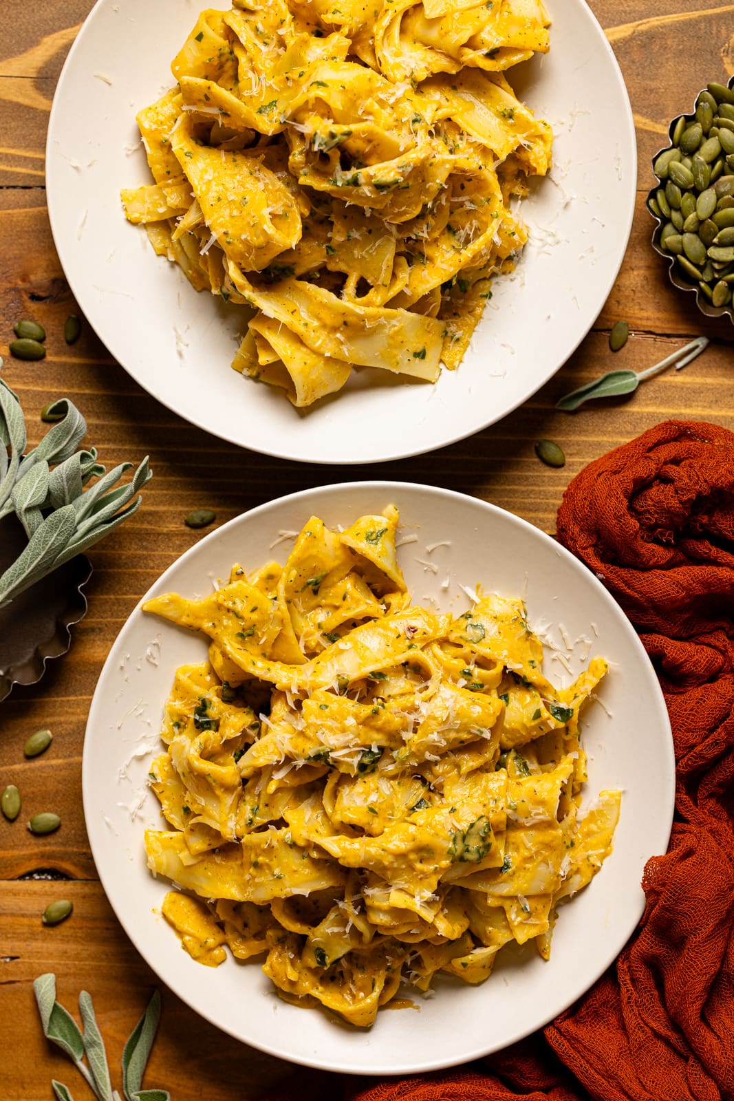 Two plates with pasta on a brown wood table with pumpkin seeds. 