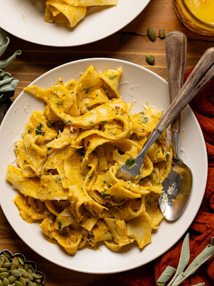 Up close shot of creamy pasta in a plate with a spoon and fork, twirled with a glass of juice.