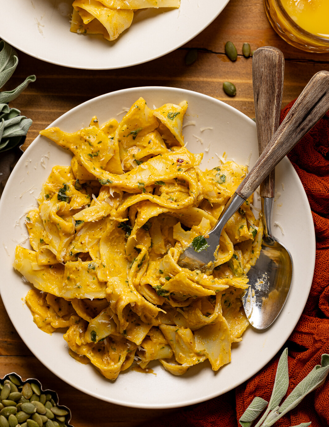 Up close shot of creamy pasta in a plate with a spoon and fork, twirled with a glass of juice. Weeknight dinner.