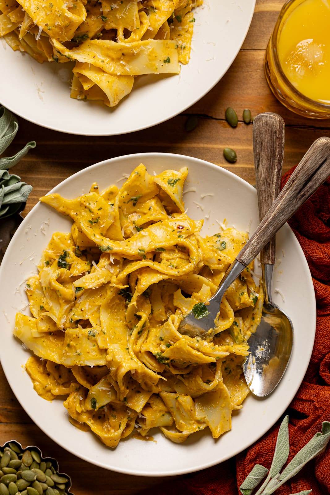 Up close shot of creamy pasta in a plate with a spoon and fork, twirled with a glass of juice. 