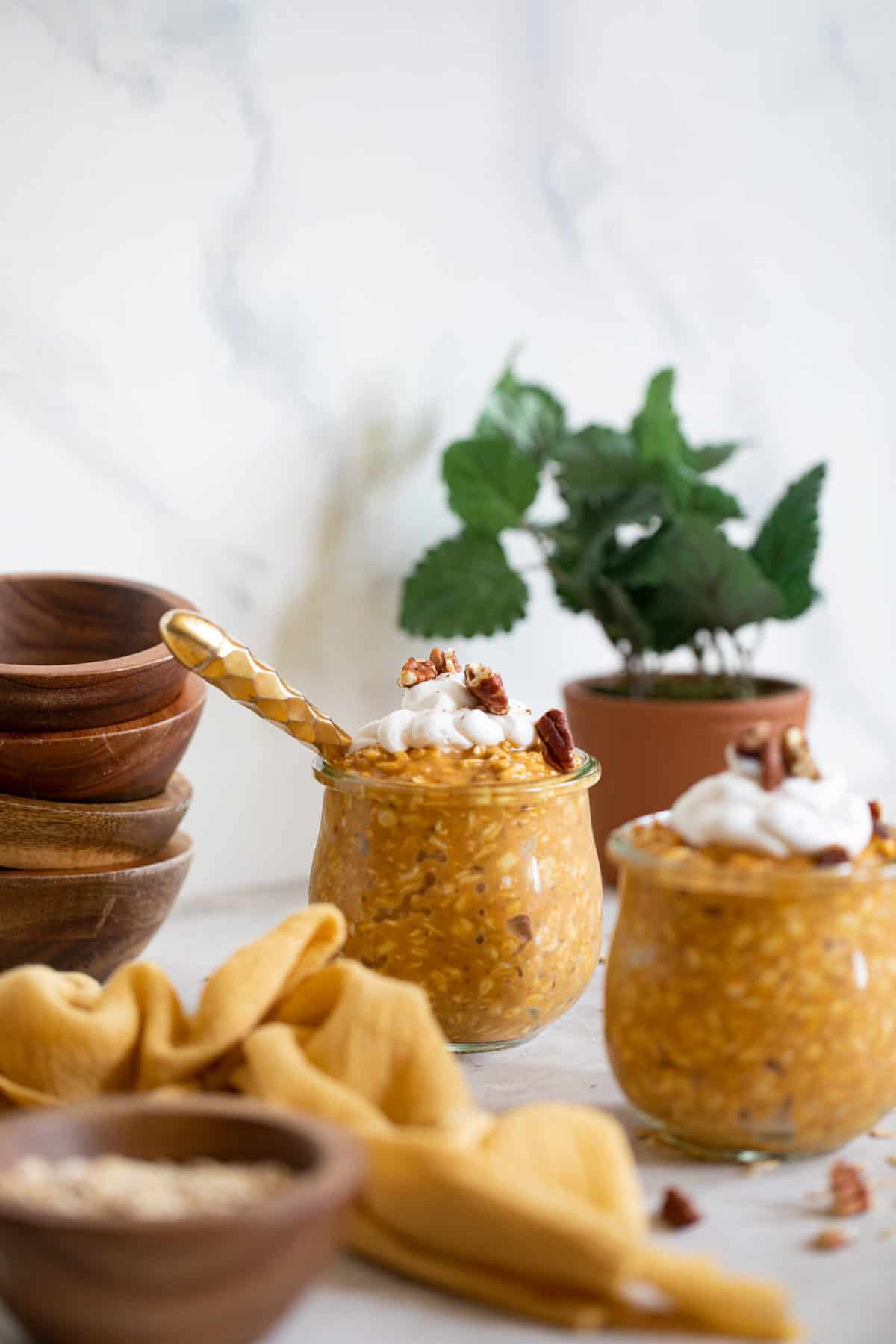 Pumpkin Spice Overnight Oats in glass jars in front of a stack of wooden bowls.