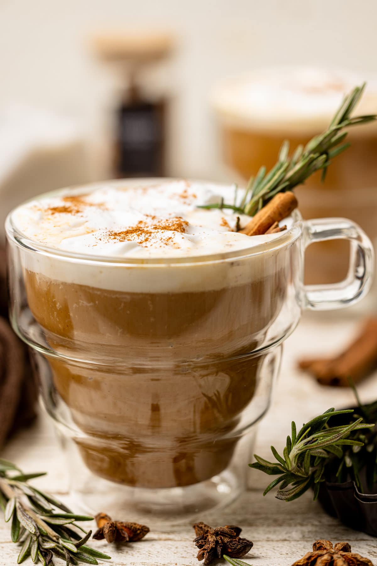 Glass mug of Vegan Pumpkin Chai Latte topped with a cinnamon stick and sprig of rosemary.