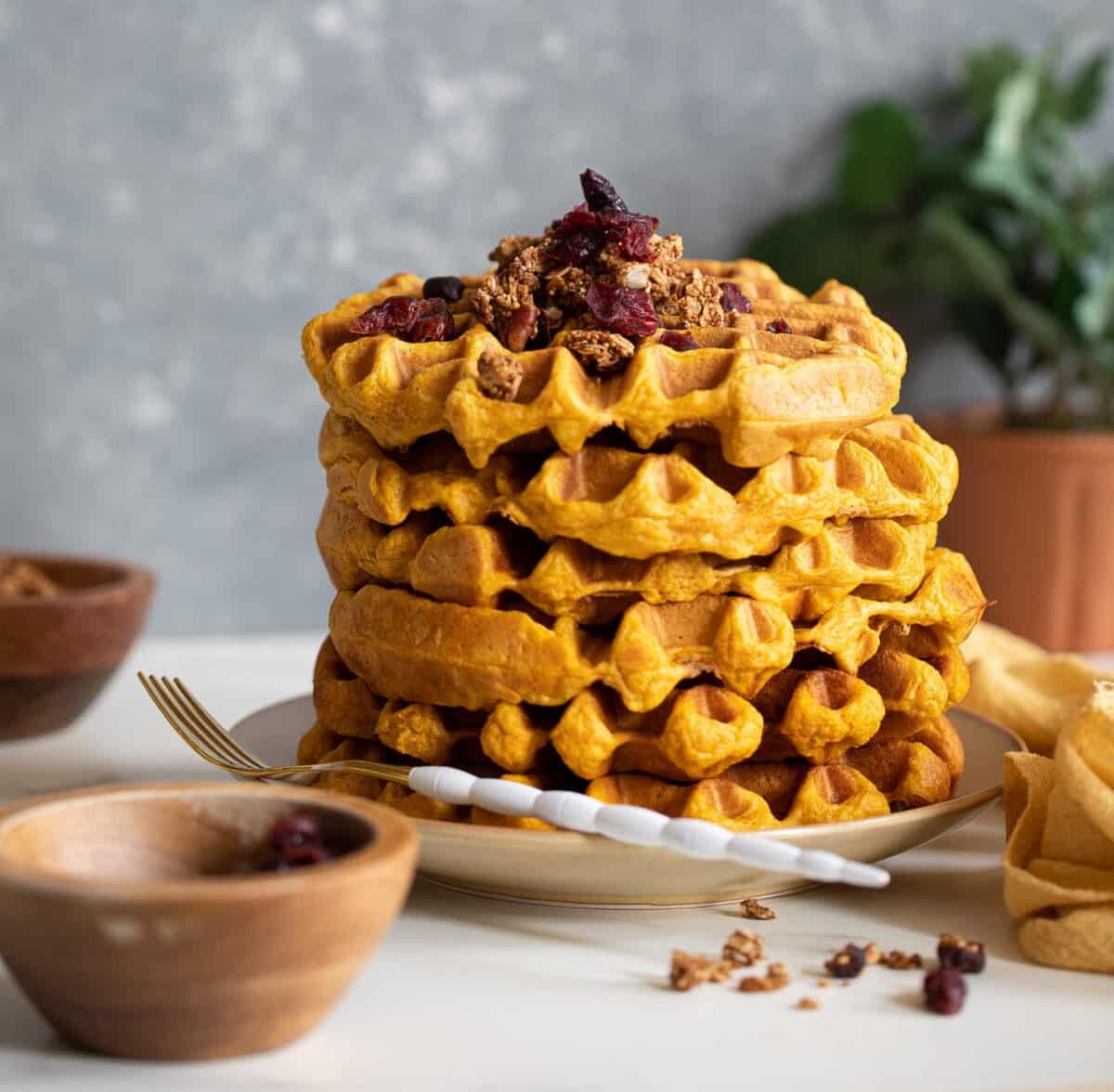 Stack of Vegan Pumpkin Spice Waffles topped with granola on a plate with a fork.