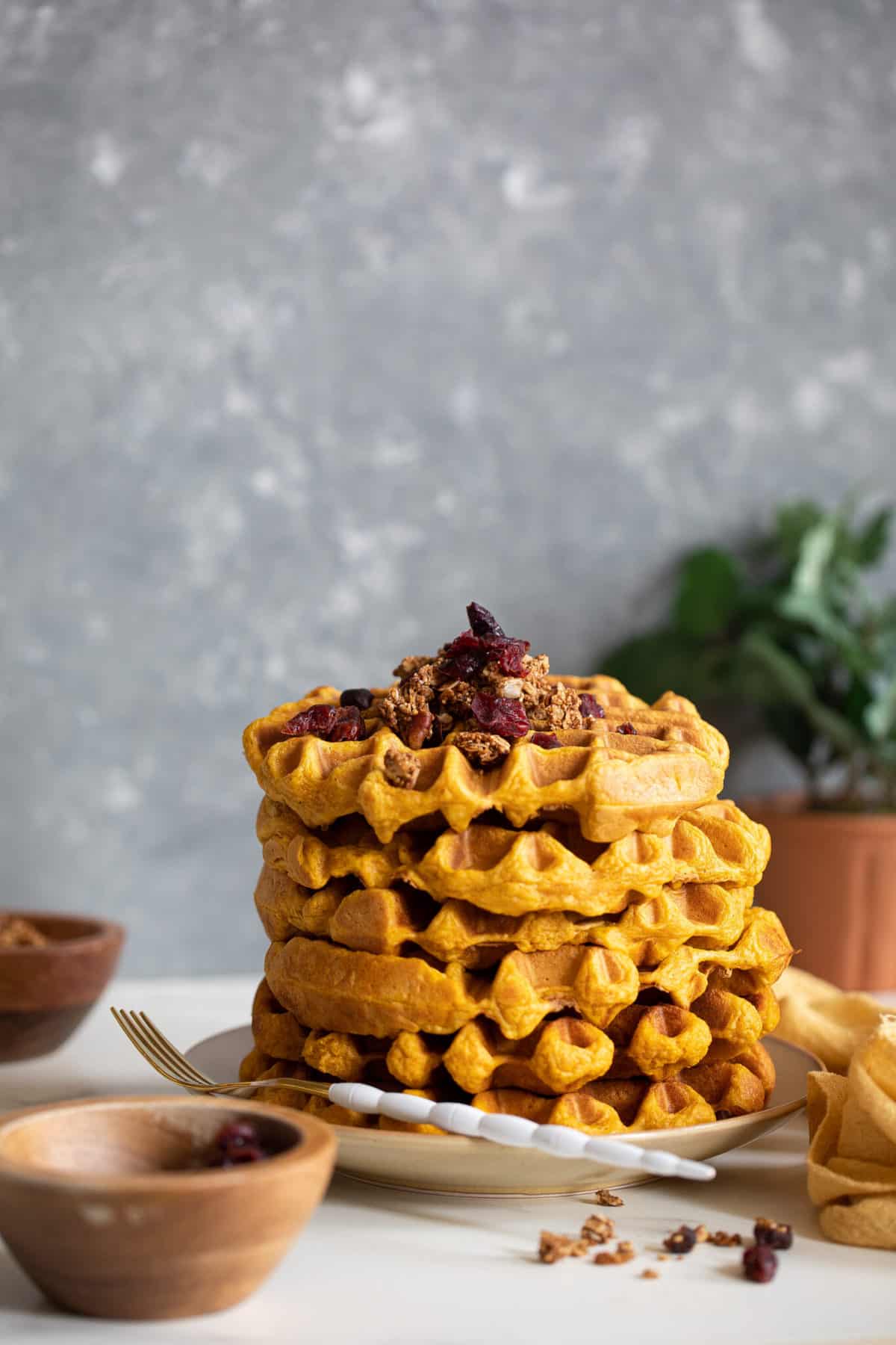 Stack of Vegan Pumpkin Spice Waffles topped with granola on a plate with a fork.