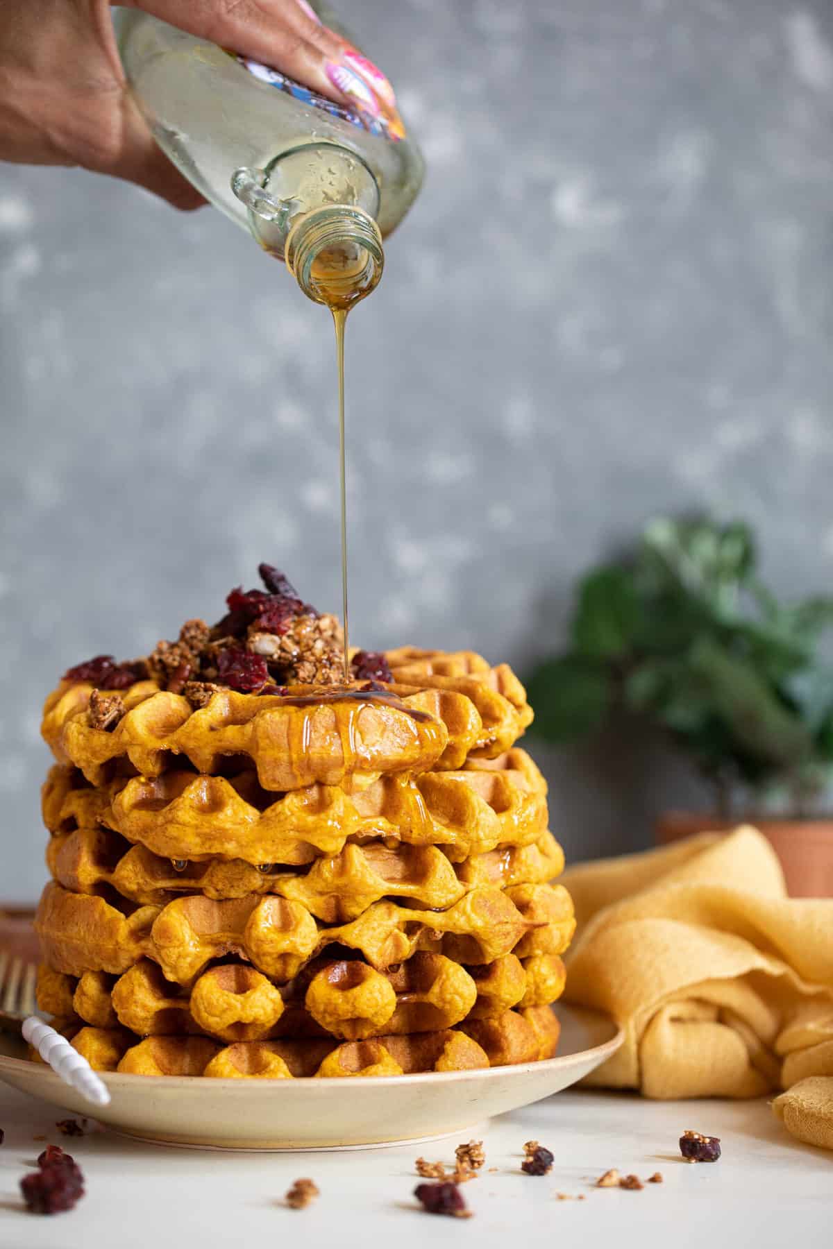 Syrup pouring onto a stack of Vegan Pumpkin Spice Waffles.