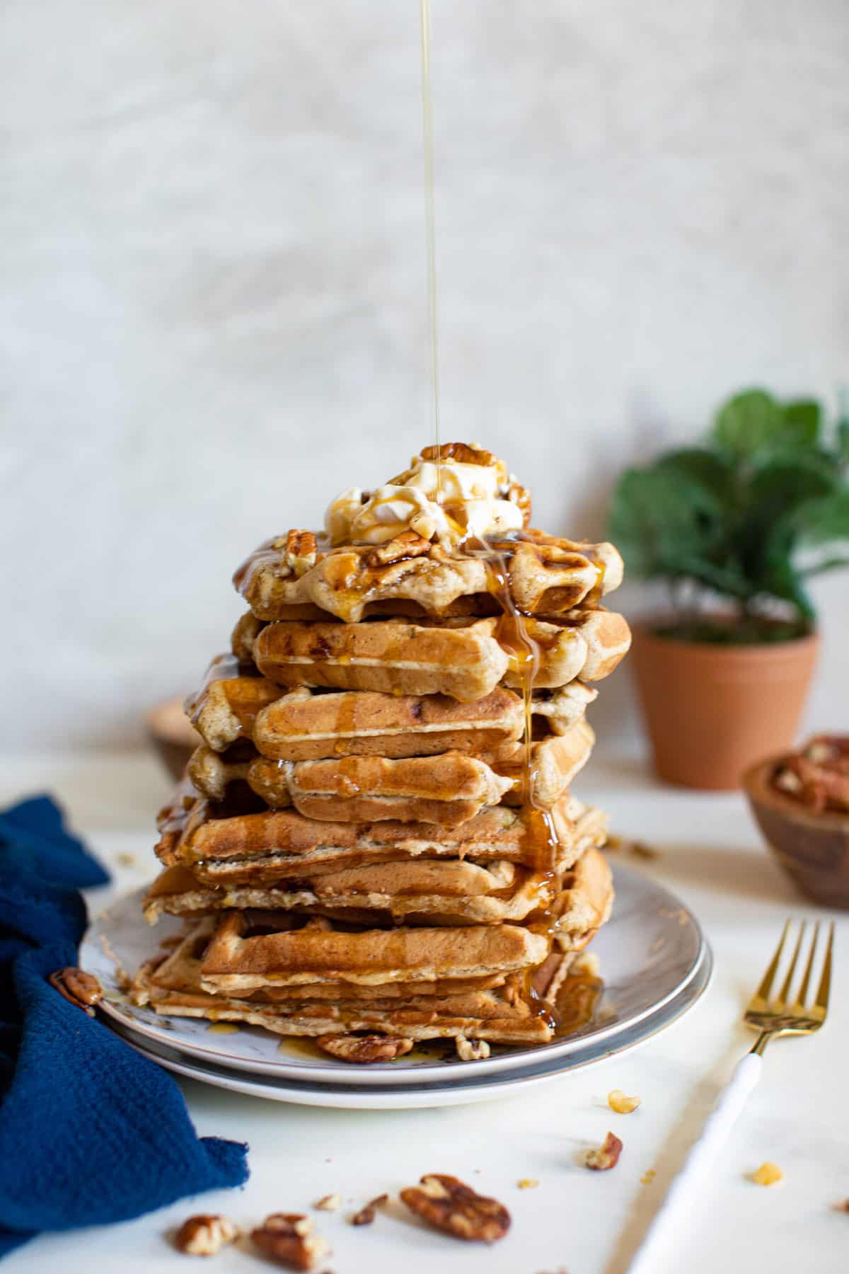 Tall stack of Maple Brown Butter Banana Waffles dripping with syrup.