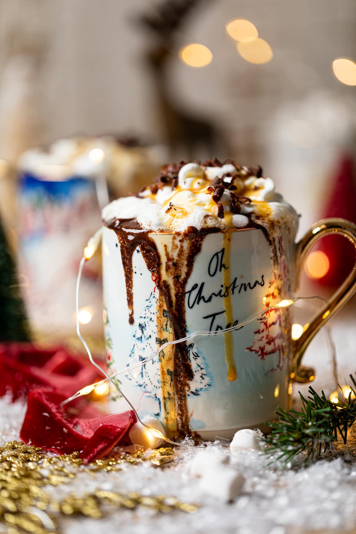 Mug that reads \"Oh Christmas Tree\" overflowing with Creamy Caramel Hot Chocolate