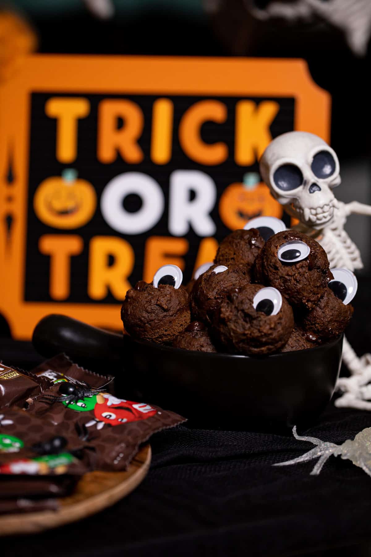 Skeleton sitting next to a bowl of cookies with googly eyes.