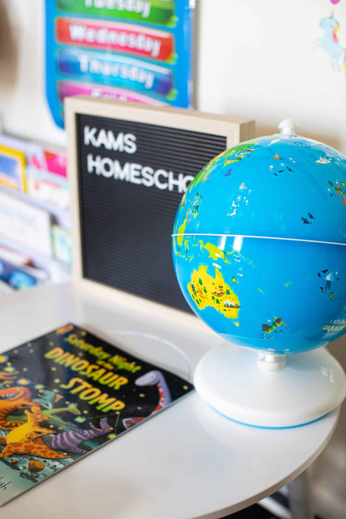 White table set with a globe, \"Dinosaur Stomp\" the book, and a sign that says \"Kams Homeschool.\"