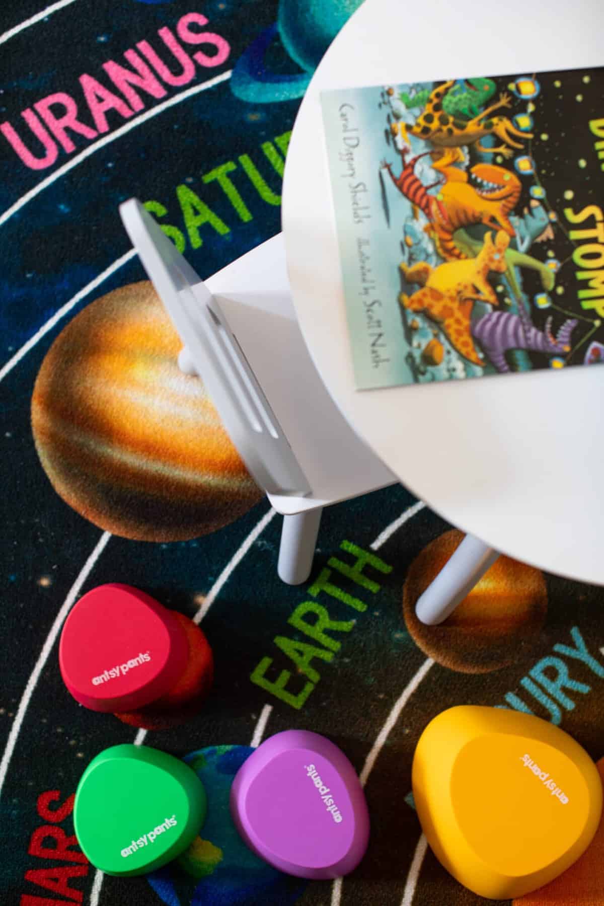 Small white table and colorful antsy pants stepping stones set on a rug with the planets.