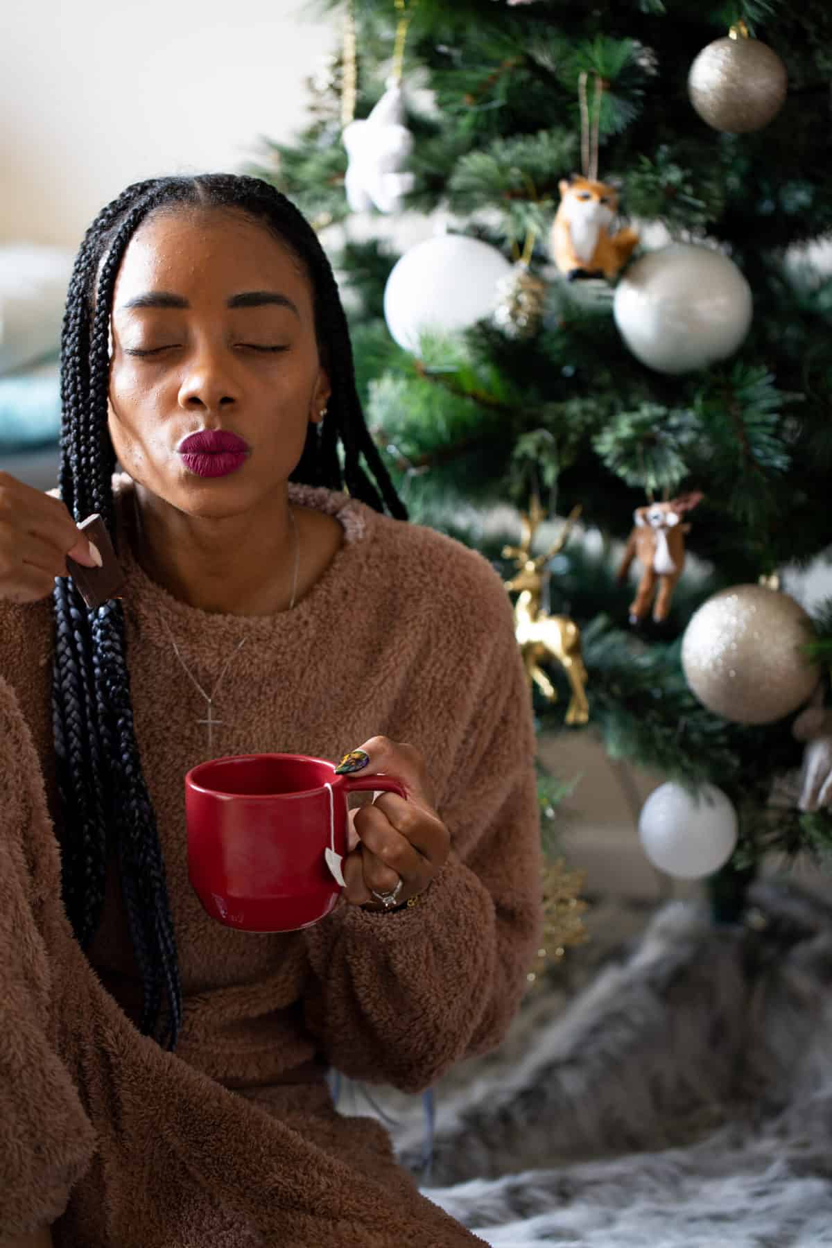 Shanika with her eyes closed and holding a red mug.