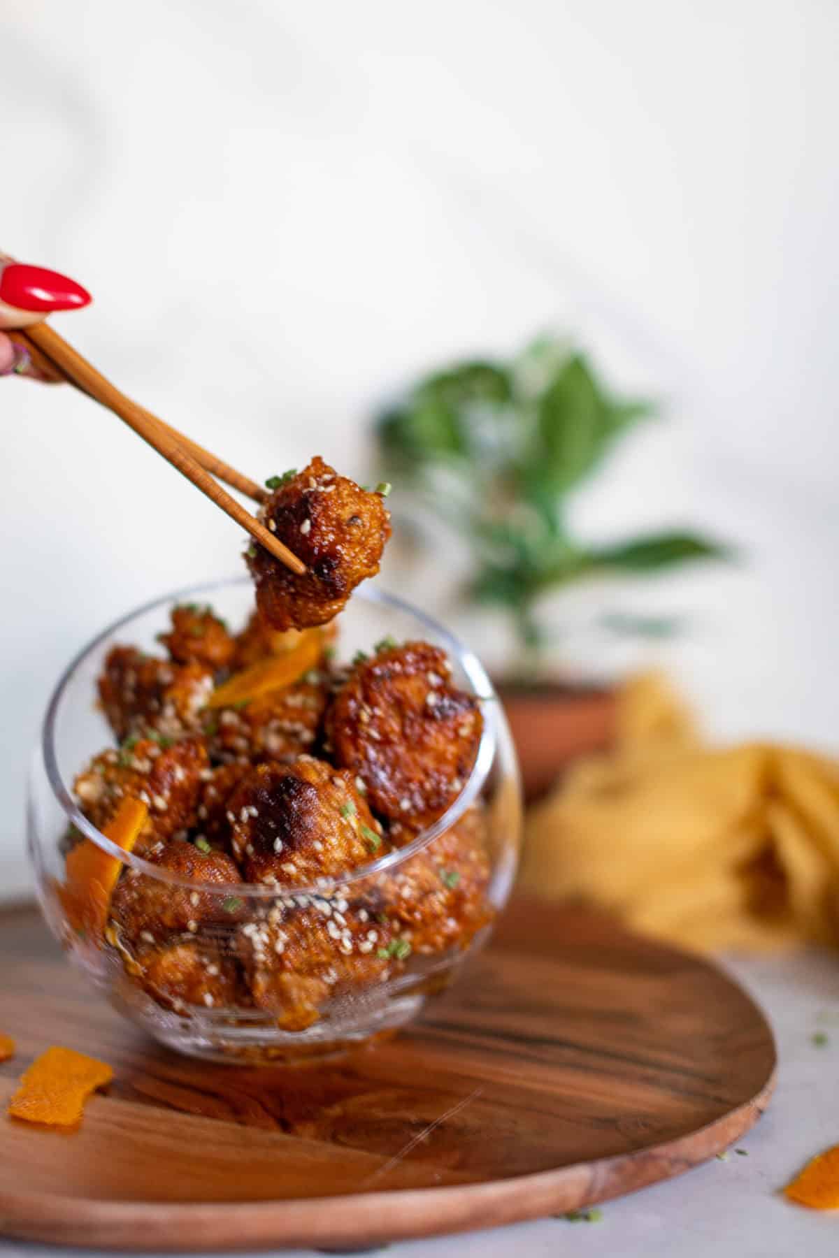 Woman using chopsticks to grab a Crispy Baked Sticky Orange Cauliflower Bite.